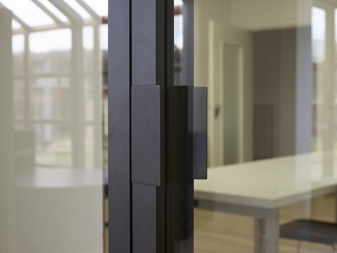 Zwarte glazen scheidingswand gecombineerd met glazen draaideur (product: divina ARLU) geïnstalleerd bij Renson Academy. 